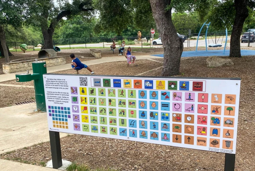Example outdoor communication board beside a playground, with colorful picture-and-word symbols that people can point to.