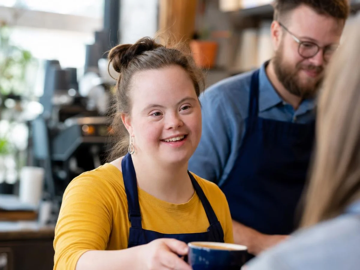 An adult woman with Down syndrome works behind the counter at a coffee shop.